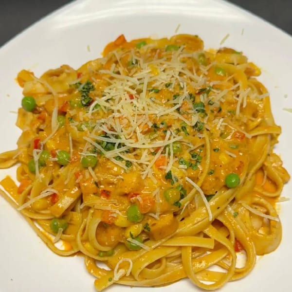Peruvian fettuccine with creamy orange sauce, green peas, and shredded cheese on a white plate.