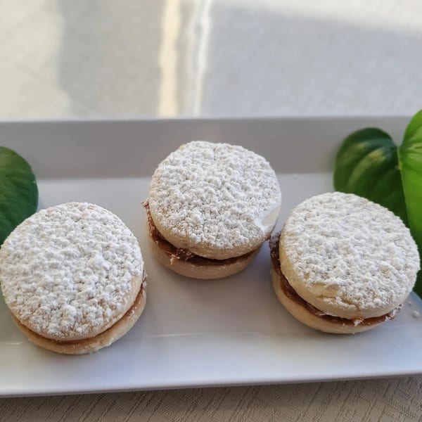 Three Peruvian alfajores, round shortbread cookies filled with dulce de leche and dusted with powdered sugar.