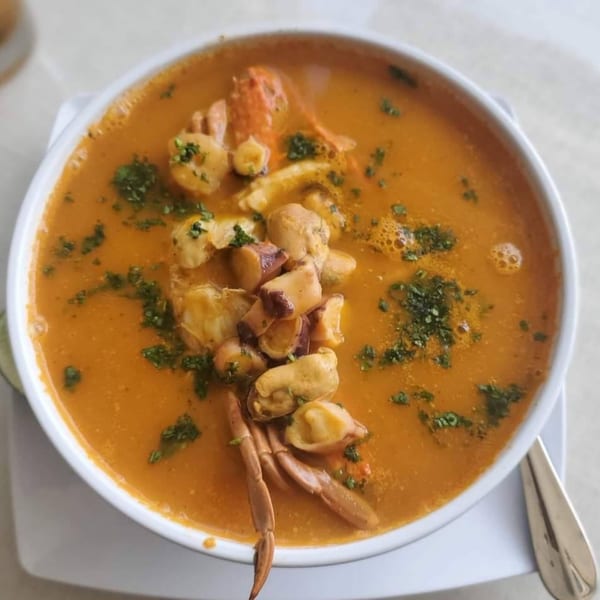 A vibrant orange Peruvian seafood soup, featuring shrimp, mussels, and crab, garnished with fresh herbs.