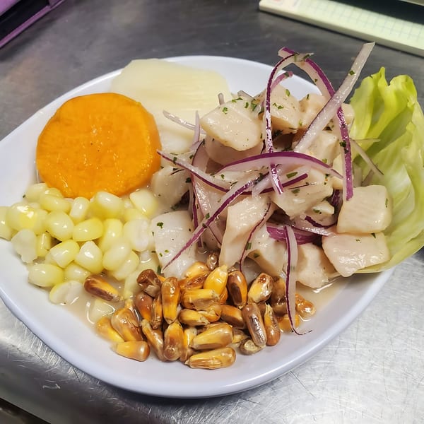 Peruvian ceviche with white fish, red onion, corn, sweet potato, and lettuce on a white plate.