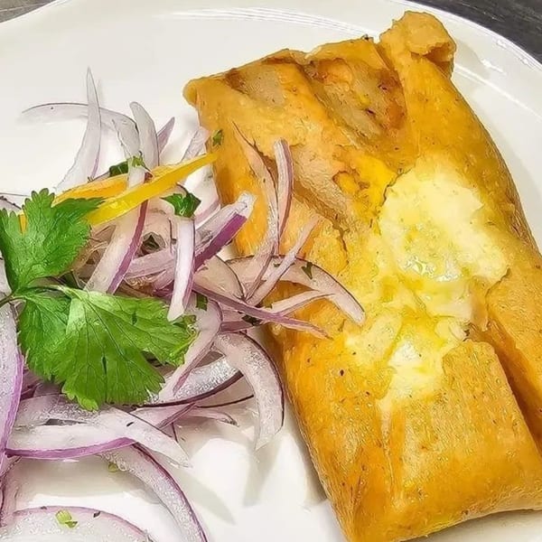 Peruvian tamale with a side of red onion, yellow pepper, and cilantro on a white plate.