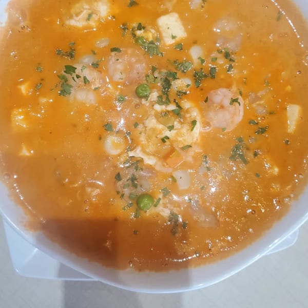 Peruvian shrimp stew with peas, cheese, and herbs in a white bowl.