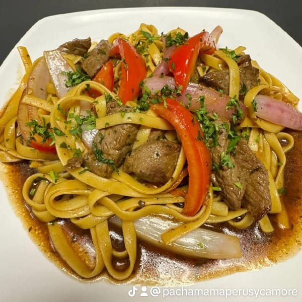 Peruvian Lomo Saltado with fettuccine, beef, red onions, bell peppers, and parsley on a white plate.