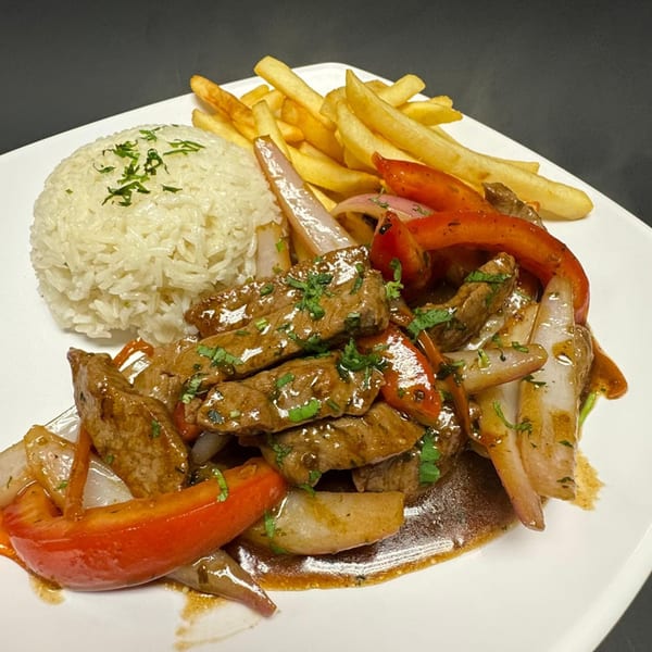 Peruvian Lomo Saltado with beef, red peppers, onions, rice, and french fries on a white plate.