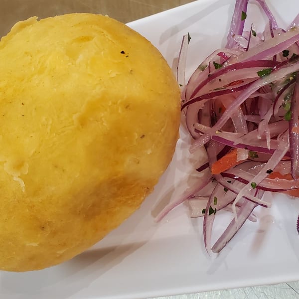 Peruvian papa rellena, a fried potato ball, served with a side of red onion relish.