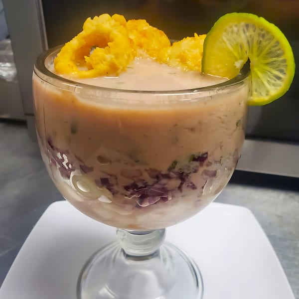 Peruvian leche de tigre cocktail with red onions, corn, and a lime wedge in a glass.